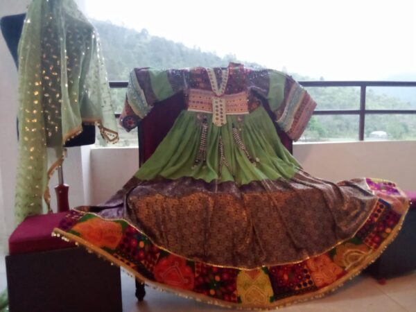 Bridal Afghani Frock in deep green velvet featuring ornate gold and purple embroidery, displayed on a mannequin beside a second traditional garment with shimmering sequins—showcasing handcrafted elegance and cultural symbolism.