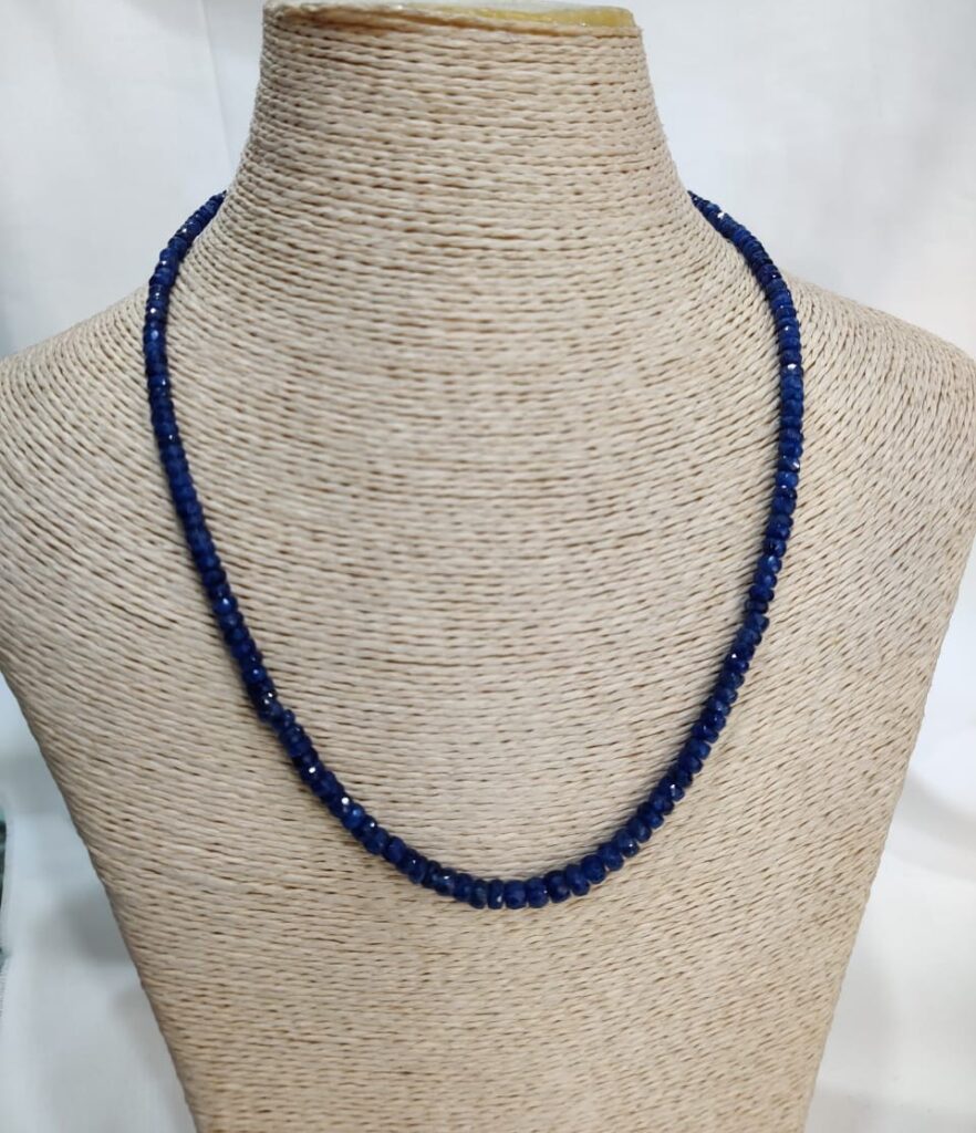 Handcrafted sapphire necklace with faceted blue beads displayed on a neutral woven bust, highlighting Afghan gemstone artistry and emotional symbolism.