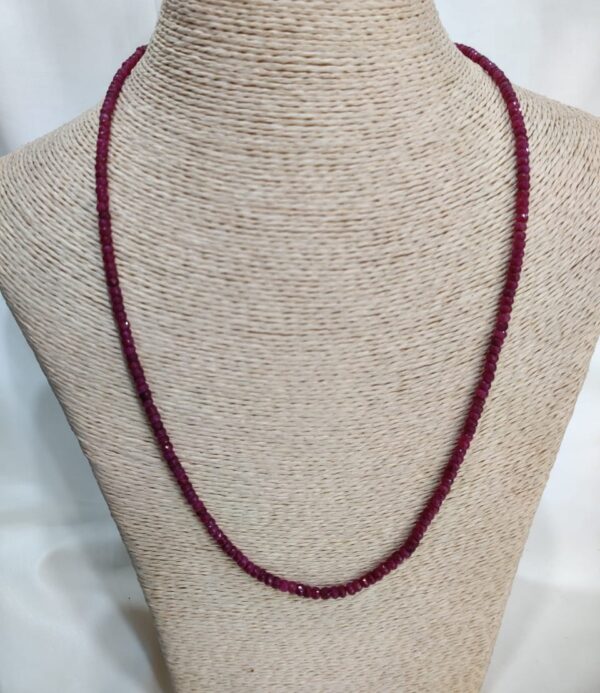 The Red Spark Ruby Necklace, featuring uniformly polished deep red beads, is elegantly displayed on a textured beige mannequin bust. Each bead reflects the vivid crimson glow of natural ruby, forming a graceful and refined design that highlights the timeless allure of the Red Spark Ruby Necklace.