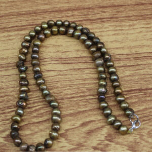 A handcrafted necklace of dark, naturally irregular lustrous pearls, elegantly arranged on a warm-toned wooden surface. Each pearl glows with a metallic sheen and organic charm, reflecting artisanal beauty and earthy sophistication.