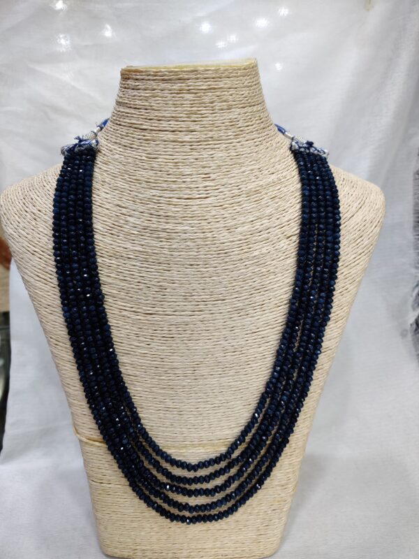 Multi-strand spinal ruby necklace displayed on a beige woven bust. The strands feature rich, deep red spinal ruby beads arranged in elegant layers, radiating warmth and sophistication.