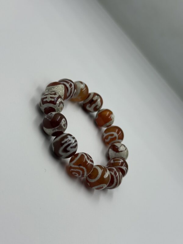 Close-up of a natural Sulimani agate bracelet showing polished beads with intricate layered patterns in earthy tones of white, grey, chocolate brown, and black, tied with