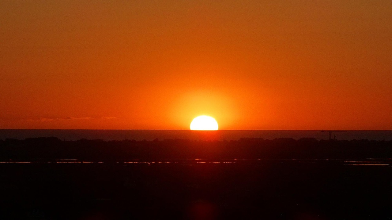 Sunset over a quiet horizon with silhouetted buildings and a crane, symbolizing reflection, transition, and the serenity of prayer in motion.
